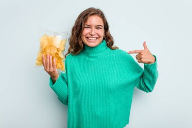 Mavi arka planda patates cipsleri tutan beyaz bir kadın tişört fotokopi alanını işaret ediyor, gururlu ve kendinden emin.