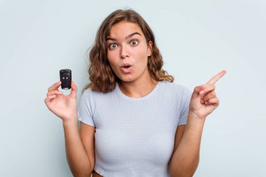 Young caucasian woman holding car keys isolated on blue background having some great idea, concept of creativity.