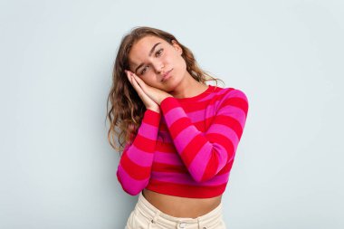 Mavi arka planda izole edilmiş genç beyaz kadın esniyor. Ağzı eliyle kapatan yorgun bir hareket sergiliyor..