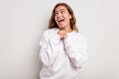 Kafkasyalı genç bir kadın mavi arka planda izole edilmiş şans için dua ediyor, şaşırmış ve ağzını açıp önüne bakıyor..