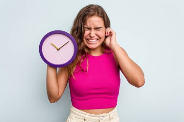 Elinde saat tutan beyaz bir kadın mavi arka planda izole edilmiş kulakları elleriyle kapatıyor..