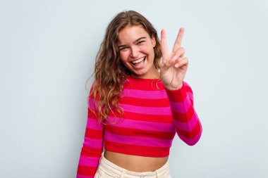 Mavi arka planda izole edilmiş genç beyaz kadın iki numarayı parmaklarıyla gösteriyor..