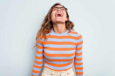 Genç beyaz kadın mavi arka planda izole edilmiş rahat ve mutlu bir şekilde gülüyor, boynunda dişlerini gösteriyor..