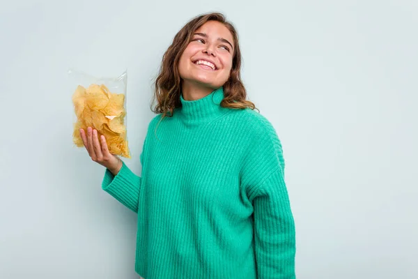 年轻的高加索女人拿着蓝色背景的土豆卷 面带微笑 快乐而愉快地把它放在一边 — 图库照片