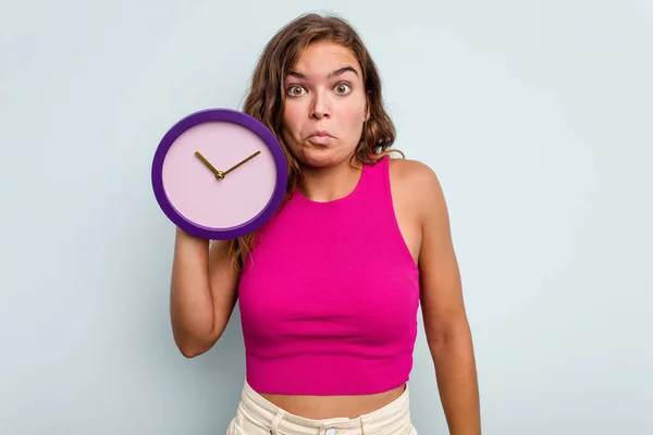 Mujer Joven Caucásica Sosteniendo Reloj Aislado Sobre Fondo Azul Encoge —  Fotos de Stock