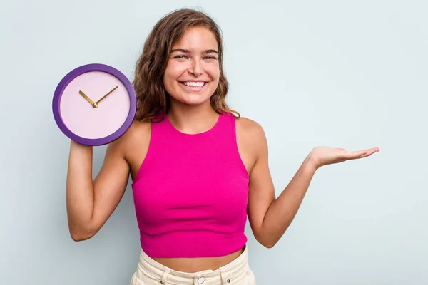 Mujer Caucásica Joven Sosteniendo Reloj Aislado Sobre Fondo Azul Mostrando —  Fotos de Stock