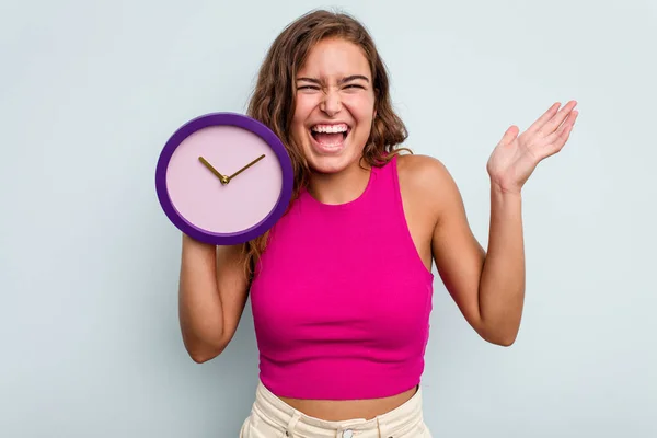 Joven Mujer Caucásica Sosteniendo Reloj Aislado Sobre Fondo Azul Recibiendo —  Fotos de Stock