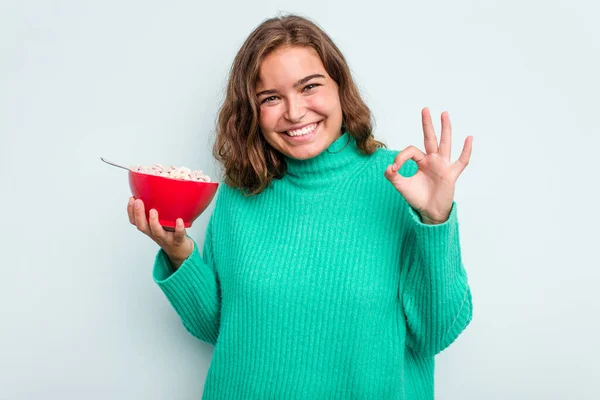 年轻的高加索女人拿着一碗谷类食品 蓝色背景隔离 快乐而自信地摆出一副不错的姿势 — 图库照片