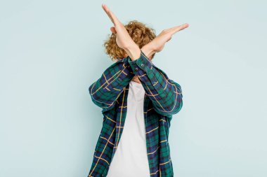 Kafkasyalı genç adam mavi arka planda izole edilmiş iki kolu çapraz tutuyor, inkar kavramı.