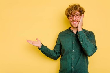 Sarı arka planda izole edilmiş genç beyaz bir adam bir avuç içinde fotokopi alanı tutuyor, el üstünde tutuyor. Şaşırmış ve mutlu..