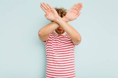 Kafkasyalı genç adam mavi arka planda izole edilmiş iki kolu çapraz tutuyor, inkar kavramı.