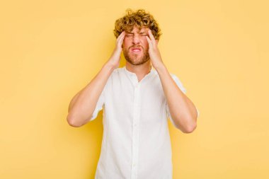 Sarı arka planda izole edilmiş genç beyaz adam tapınaklara dokunuyor ve baş ağrısı çekiyor..