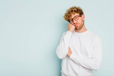 Mavi arka planda izole edilmiş, üzgün ve dalgın hisseden, kopyalama alanına bakan genç beyaz bir adam..