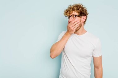 Kafkasyalı genç adam mavi arka planda izole edilmiş. Düşünceli bir şekilde ağzıyla ağzını kapatan bir fotokopi odasına bakıyor..