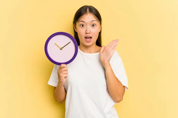 Young Asian Woman Holding Clock Isolated Yellow Background Surprised Shocked — Stock Photo, Image