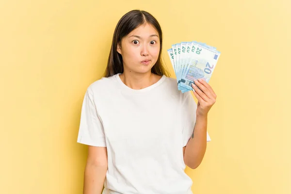 Young Asian Woman Holding Banknotes Isolated Yellow Background Shrugs Shoulders — Stock Photo, Image