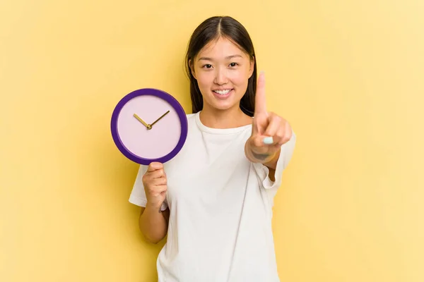 Jovem Mulher Asiática Segurando Relógio Isolado Fundo Amarelo Mostrando Número — Fotografia de Stock