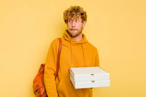 Młody Student Trzymający Pizzę Żółtym Tle Czuje Się Zdezorientowany Wątpi — Zdjęcie stockowe