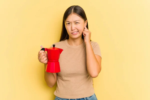 Młoda Azjatka Trzyma Ekspres Kawy Odizolowany Żółtym Tle Pokrywa Uszy — Zdjęcie stockowe