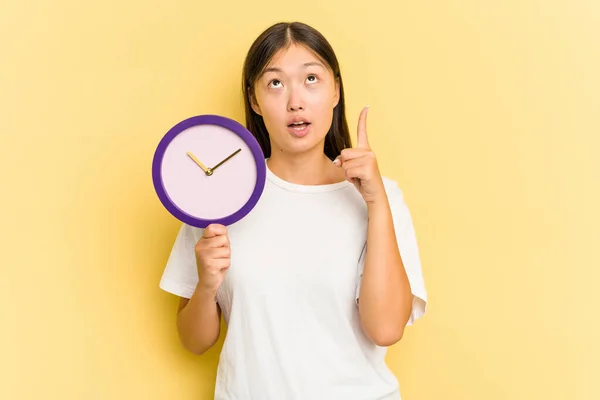 Young Asian Woman Holding Clock Isolated Yellow Background Pointing Upside — Stock Photo, Image