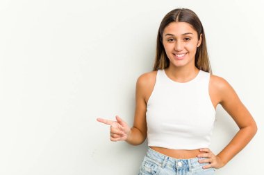 Beyaz arka planda izole edilmiş genç Hintli kadın işaret parmağıyla işaret ederek gülümsüyor..