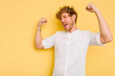 Sarı arka planda izole edilmiş genç beyaz adam zaferden sonra yumruğunu kaldırıyor, kazanan konsept..