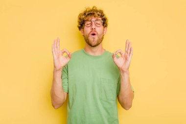 Sarı arka planda izole edilmiş genç beyaz adam sıkı çalışma gününden sonra rahatlıyor. Yoga yapıyor..