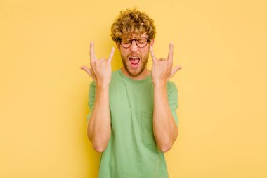 Sarı arka planda izole edilmiş genç beyaz adam boynuzlarını devrim konsepti olarak gösteriyor..