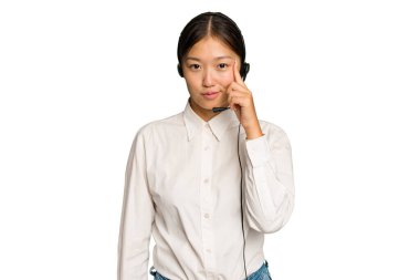 Tele pazarlamacı Asyalı kadın yeşil renkli arka planda izole edilmiş bir kulaklıkla çalışıyor. Şakağı işaret ediyor, düşünüyor, bir göreve odaklanıyor..