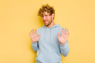 Sarı arka planda izole edilmiş genç beyaz adam tiksinti belirtisi gösteren birini reddediyor..