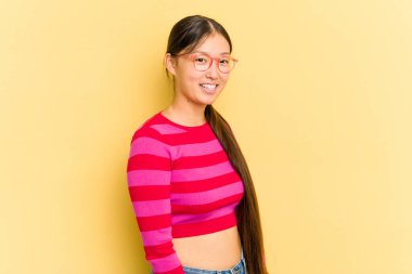 Sarı arka planda izole edilmiş genç Asyalı kadın ellerini kalçasından ayırmıyor..