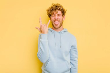 Sarı arka planda izole edilmiş genç beyaz adam parmaklarıyla kaya hareketi gösteriyor.