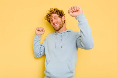 Sarı arka planda izole edilmiş genç beyaz adam özel bir günü kutluyor, atlıyor ve enerjiyle kollarını kaldırıyor..