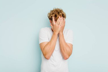 Kafkasyalı genç adam mavi arka planda izole edilmiş. Korkmuş ve gergin parmaklarıyla göz kırp..