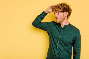 Kafkasyalı genç adam sarı arka planda izole edilmiş, uzaklara bakıyor ve elini alnına koyuyor..