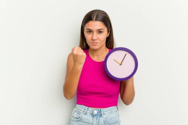 Elinde beyaz arka planda izole edilmiş bir saat tutan genç Hintli kadın yumruğunu kameraya gösteriyor, agresif yüz ifadesi..
