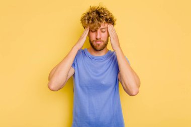 Sarı arka planda izole edilmiş genç beyaz adam tapınaklara dokunuyor ve baş ağrısı çekiyor..