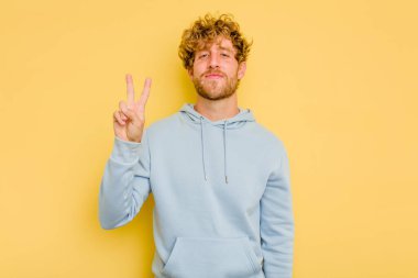 Sarı arka planda izole edilmiş genç beyaz adam neşeli ve kaygısız parmakları olan bir barış sembolü gösteriyor..
