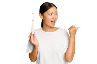 Elinde elektrikli diş fırçası tutan genç Asyalı kadın yeşil renkli arka plan noktalarından izole edilmiş, başparmak uzakta, gülen ve kaygısız..