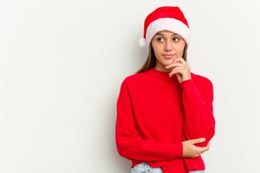 Genç Hintli kadın Noel 'i beyaz arka planda yalnız kutluyor. Şüpheli ve şüpheci bir ifadeyle yana bakıyor..