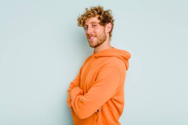 Kafkasyalı genç, mavi arka planda izole edilmiş. Kendine güvenen, kalçaları tutan biri..