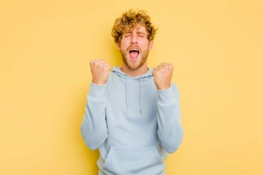 Sarı arka planda izole edilmiş genç beyaz adam tasasız ve heyecanlı bir şekilde tezahürat yapıyor. Zafer konsepti.