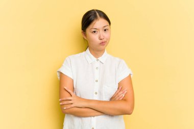 Sarı arka planda izole edilmiş genç Asyalı kadın alaycı bir ifadeyle kameraya bakıyor..