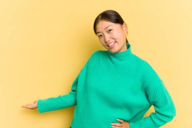 Sarı arka planda izole edilmiş genç Asyalı kadın hoş bir ifade sergiliyor..