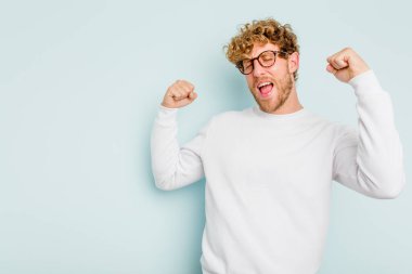 Mavi arka planda izole edilmiş genç beyaz bir adam zaferden sonra yumruğunu kaldırıyor, kazanan konsept..
