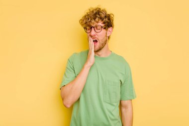 Sarı arka planda izole edilmiş genç beyaz adam esniyor. Ağzı eliyle kapatan yorgun bir hareket sergiliyor..