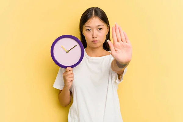 Νεαρή Ασιάτισσα Κρατώντας Ένα Ρολόι Απομονωμένο Κίτρινο Φόντο Στέκεται Τεντωμένο — Φωτογραφία Αρχείου