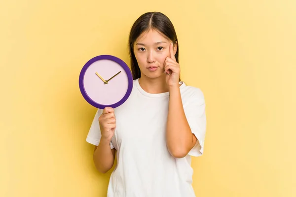 Junge Asiatische Frau Hält Eine Auf Gelbem Hintergrund Isolierte Uhr — Stockfoto