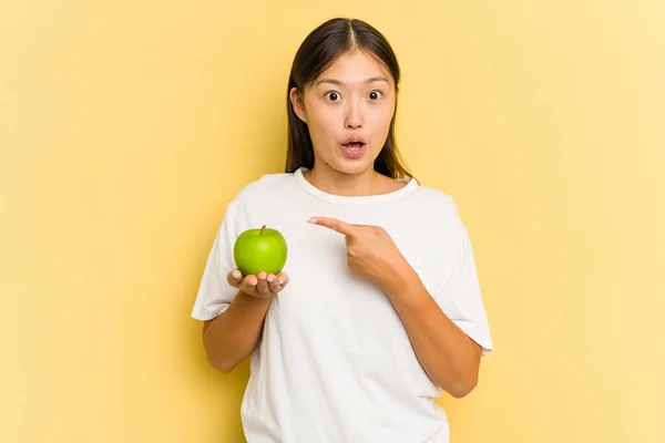 Young Asian Woman Eating Apple Isolated Yellow Background Pointing Side — Stock Photo, Image