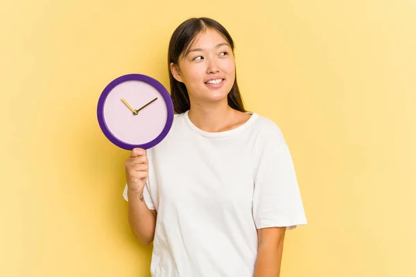 Joven Mujer Asiática Sosteniendo Reloj Aislado Sobre Fondo Amarillo Mira —  Fotos de Stock